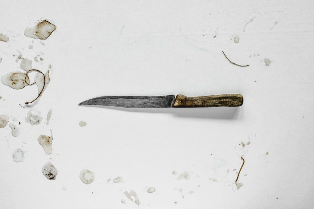 A rustic knife with a wood handle on a white surface marked with stains and debris.