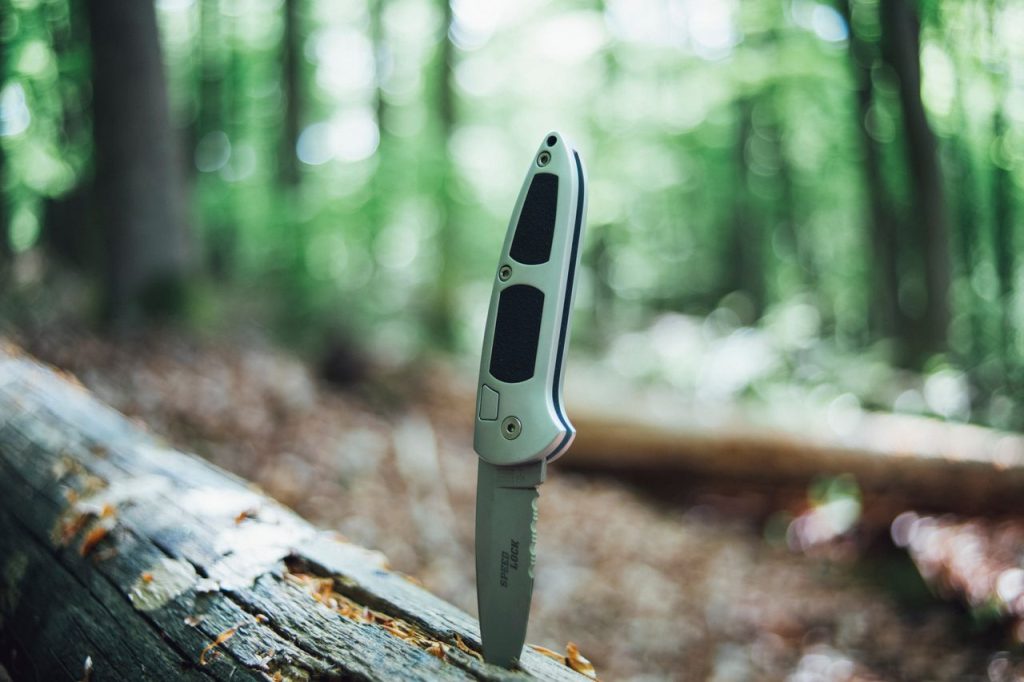 Close-up of a folding knife in a forest, symbolizing outdoor adventure and survival.