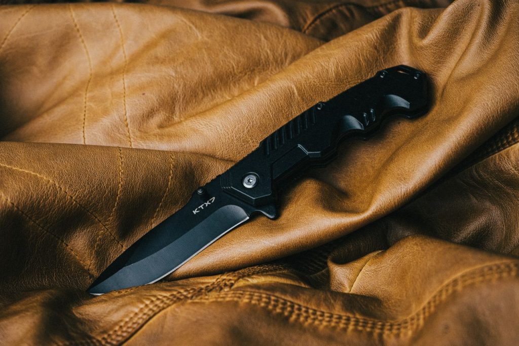 The Art of Drawing Readers In: Your attractive post title goes here A sleek black folding knife on a textured brown leather surface, showcasing its design.