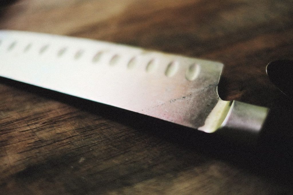 Detailed close-up of a sharp kitchen knife resting on a rustic wooden surface.